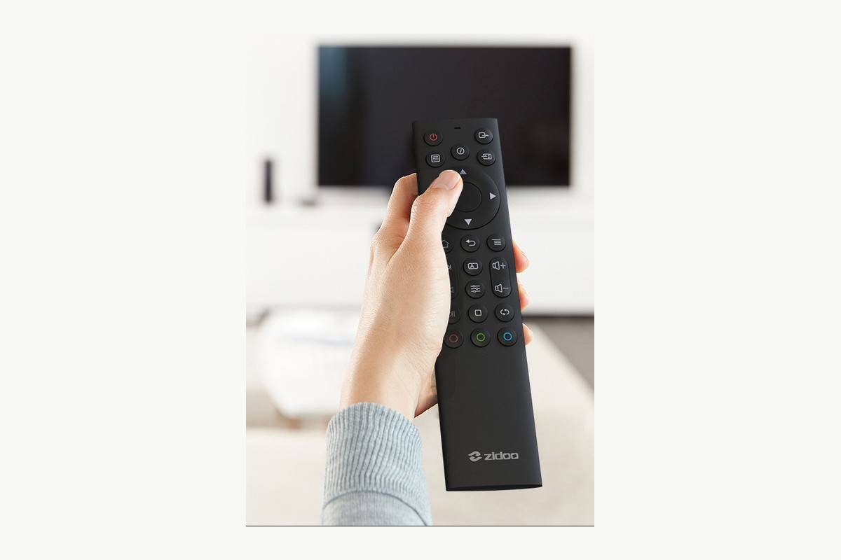 Main pointant une télécommande noire vers un téléviseur dans un salon clair